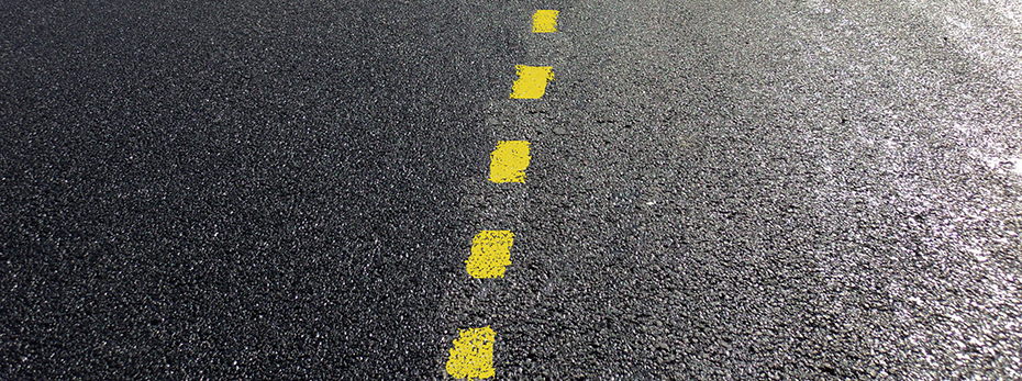 Close-up of two-lane road with yellow dashed traffic line paint going up the middle